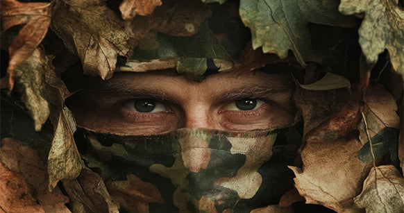 Augenpaar aus Ghillie-suit Tarnanzug schauend.