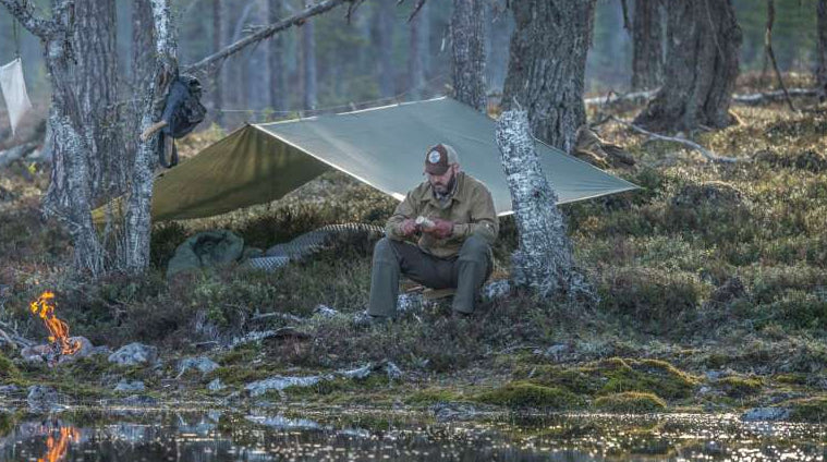 Mann mit aufgespanntem Tarp am Seeufer